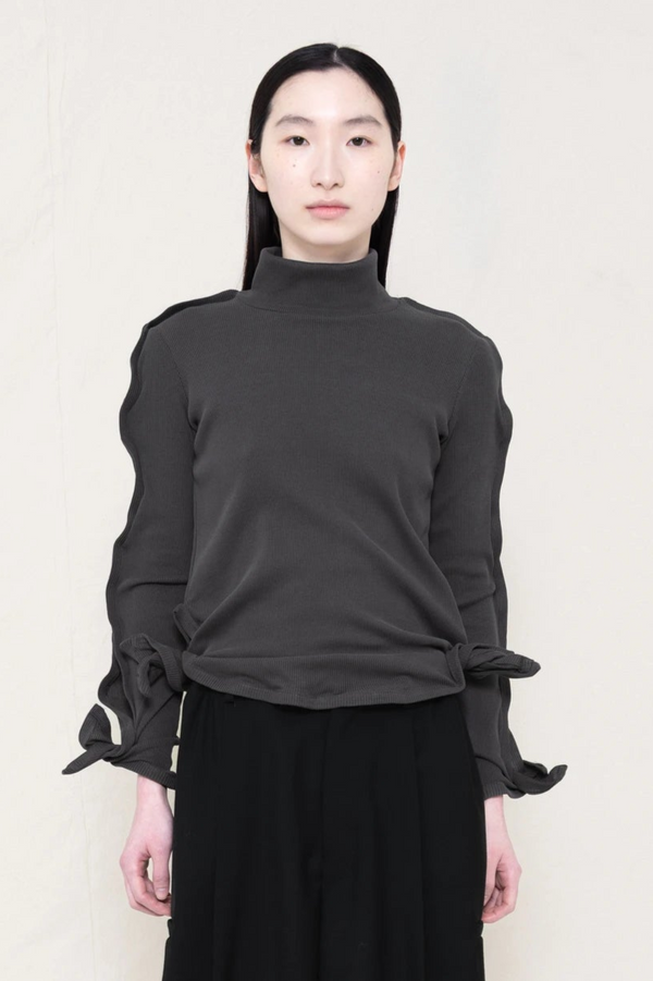 PERSON-WEARING-DARK-GREY-ZIG-ZAG-TOP-FEATURING-MALLEABLE-SLEEVES-PAIRED-WITH-BLACK-TAILORED-PANTS-CLOSE-UP-FRONT-VIEW