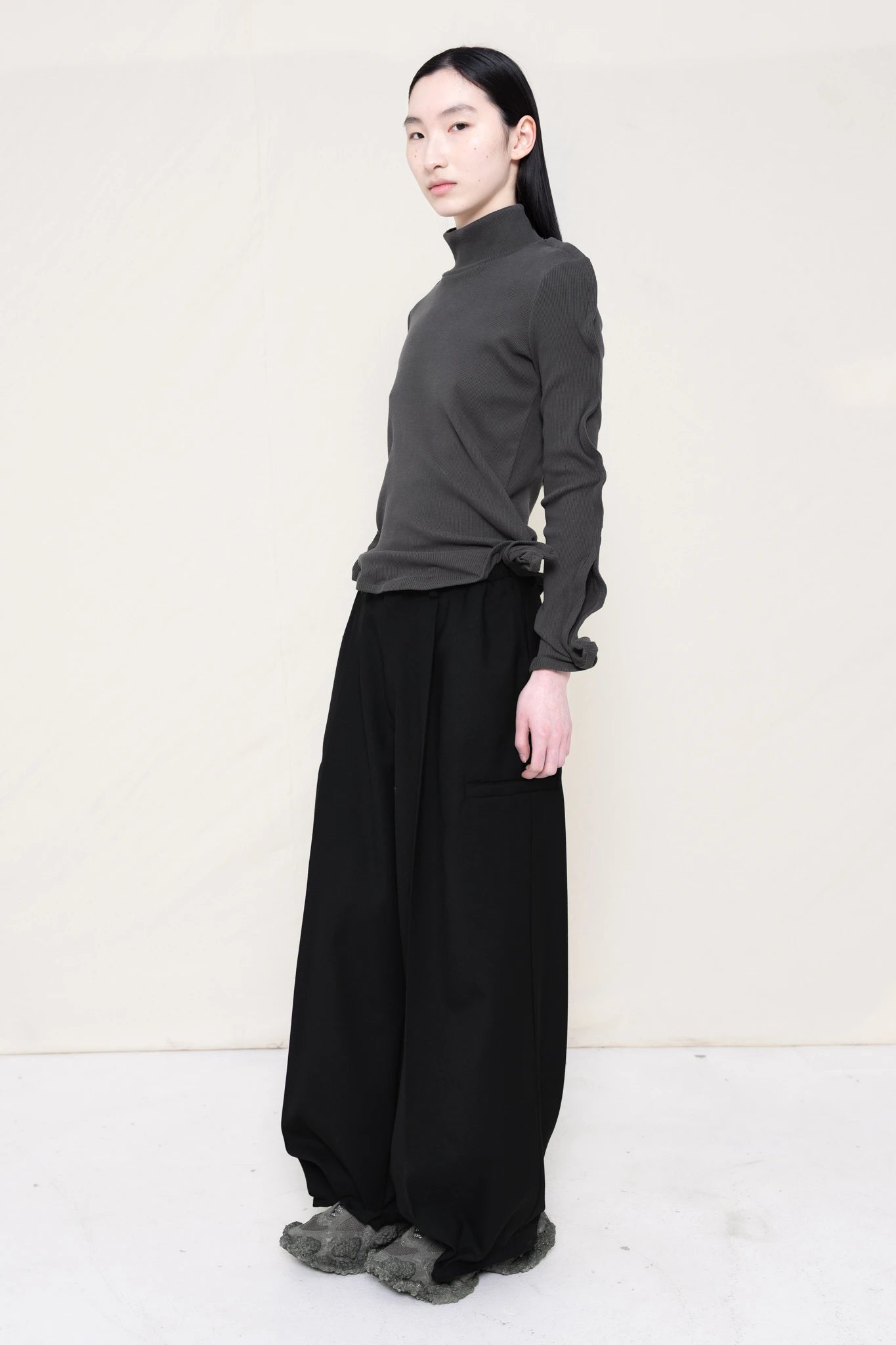 PERSON-WEARING-DARK-GREY-ZIG-ZAG-TOP-FEATURING-MALLEABLE-SLEEVES-PAIRED-WITH-BLACK-TAILORED-PANTS-AND-CUSTOMIZED-SNEAKERS-THREE-QUARTER-VIEW