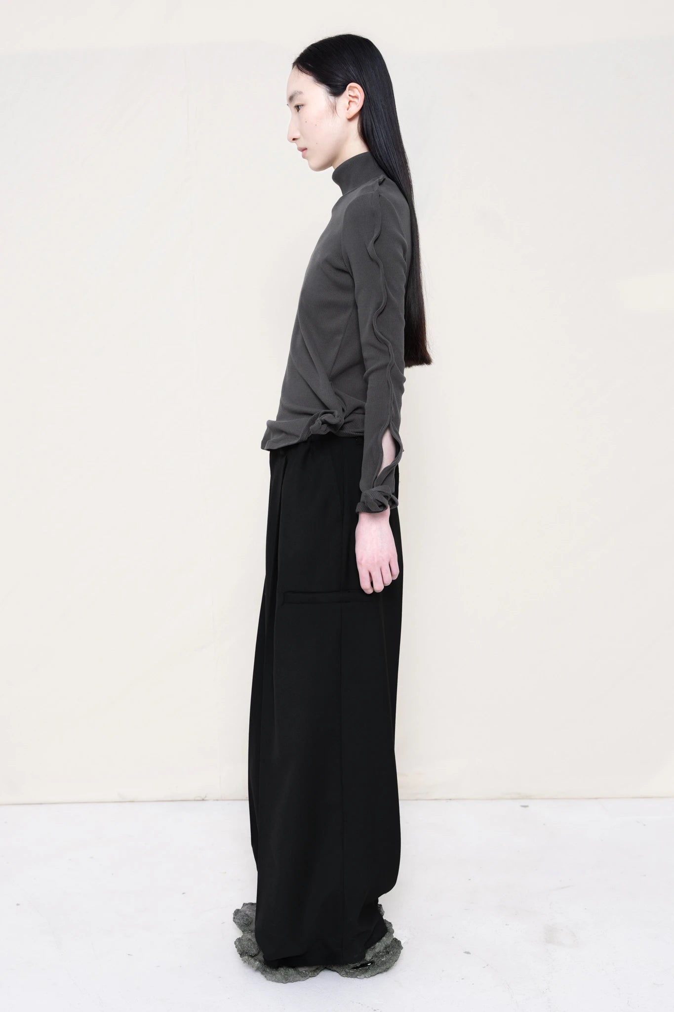 PERSON-WEARING-DARK-GREY-ZIG-ZAG-TOP-FEATURING-MALLEABLE-SLEEVES-PAIRED-WITH-BLACK-TAILORED-PANTS-AND-CUSTOMIZED-SNEAKERS-SIDE-VIEW