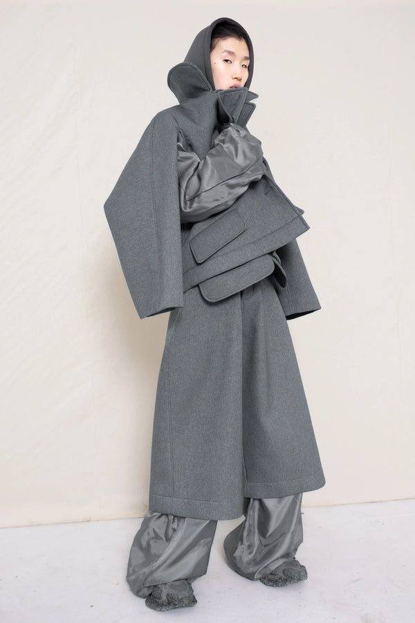 A-model-wearing-A-grey-DOUBLE-LAPEL-JACKET-WITH-grey-SILKY-SECOND-SLEEVEs-over-a-spongey-grey-hoodie-and-grey-trousers-and-silky-underlayer-draped-from-under-the-cuffs-full-body-three-quarters-view