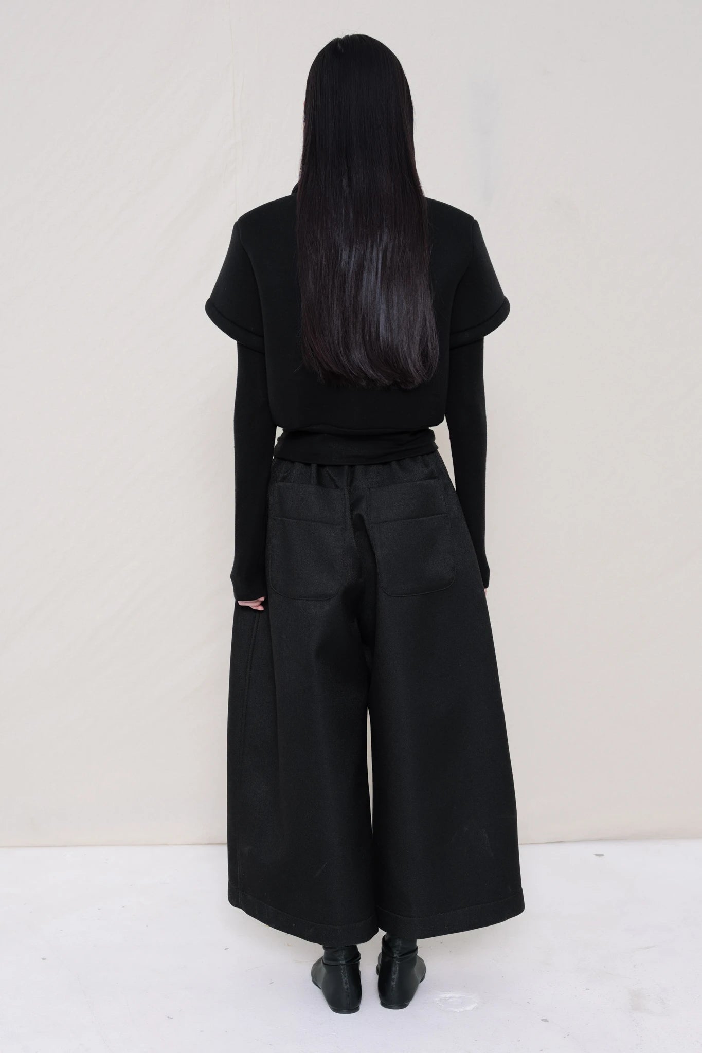 women-wearing-a-black-cropped-extremely-spongy-polo-shirt-over-a-black-turle-neck-worn-with-black-spongy-WIDE-LEG-TAILORED-WAIS-CULOTTE-PANT-paired-with-balck-pointed-leather-boots-full-body-back-view