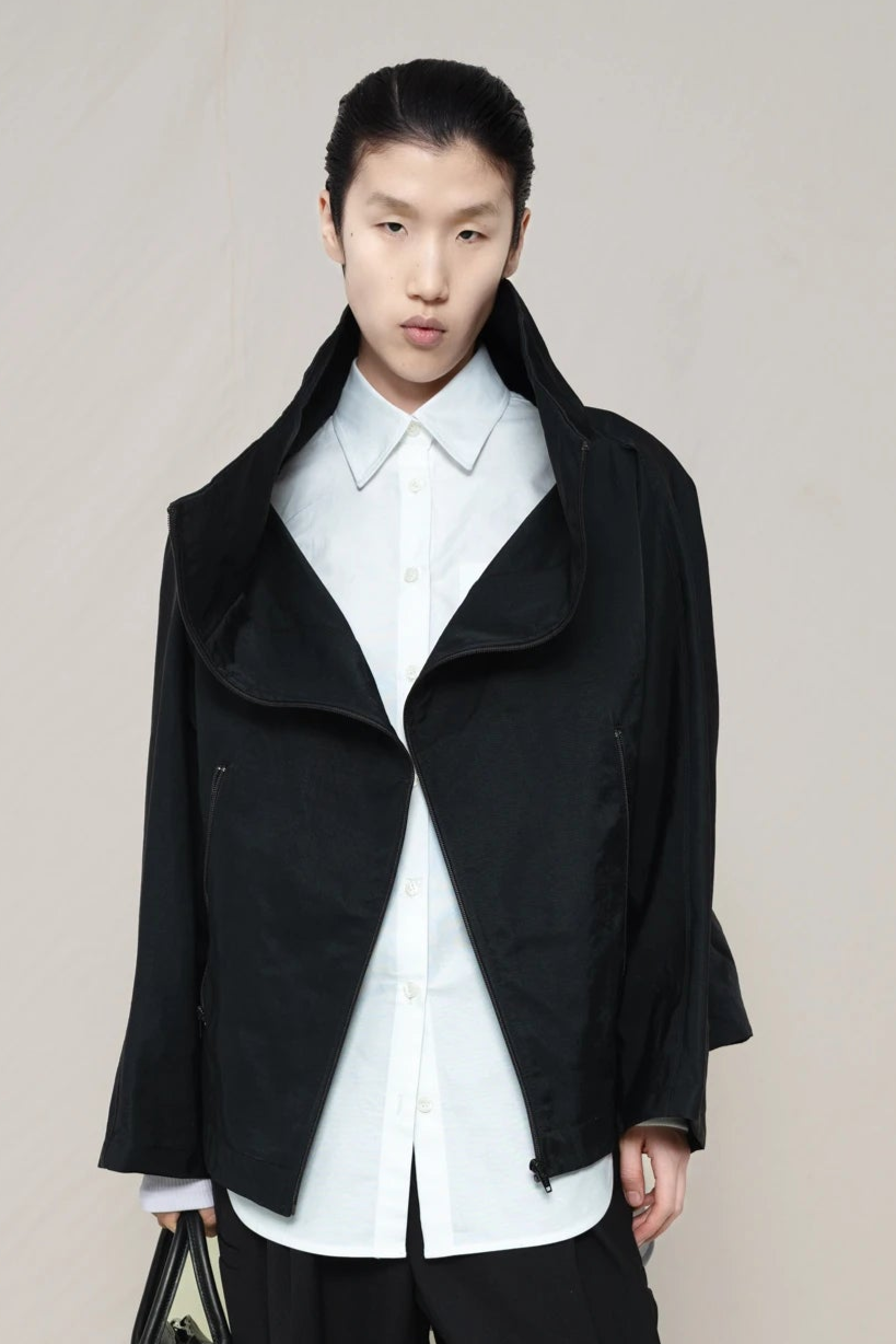 PERSON-WEARING-WHITE-SLIM-SLEEVE-BUTTON-DOWN-UNDER-BLACK-BOXY-ZIP-UP-JACKET-WITH-BLACK-TAILORED-PANTS-HOLDING-BAG-CLOSE-UP-FRONT-VIEW
