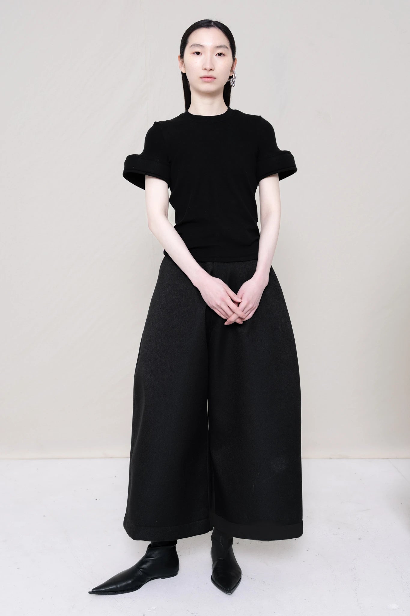 PERSON-WEARING-BLACK-TEE-WITH-FOAM-SLEEVE-CUFFS-AND-BLACK-CULOTTE-PANTS-WITH-BLACK-FLAT-POINTY-BOOTS-FRONT-VIEW