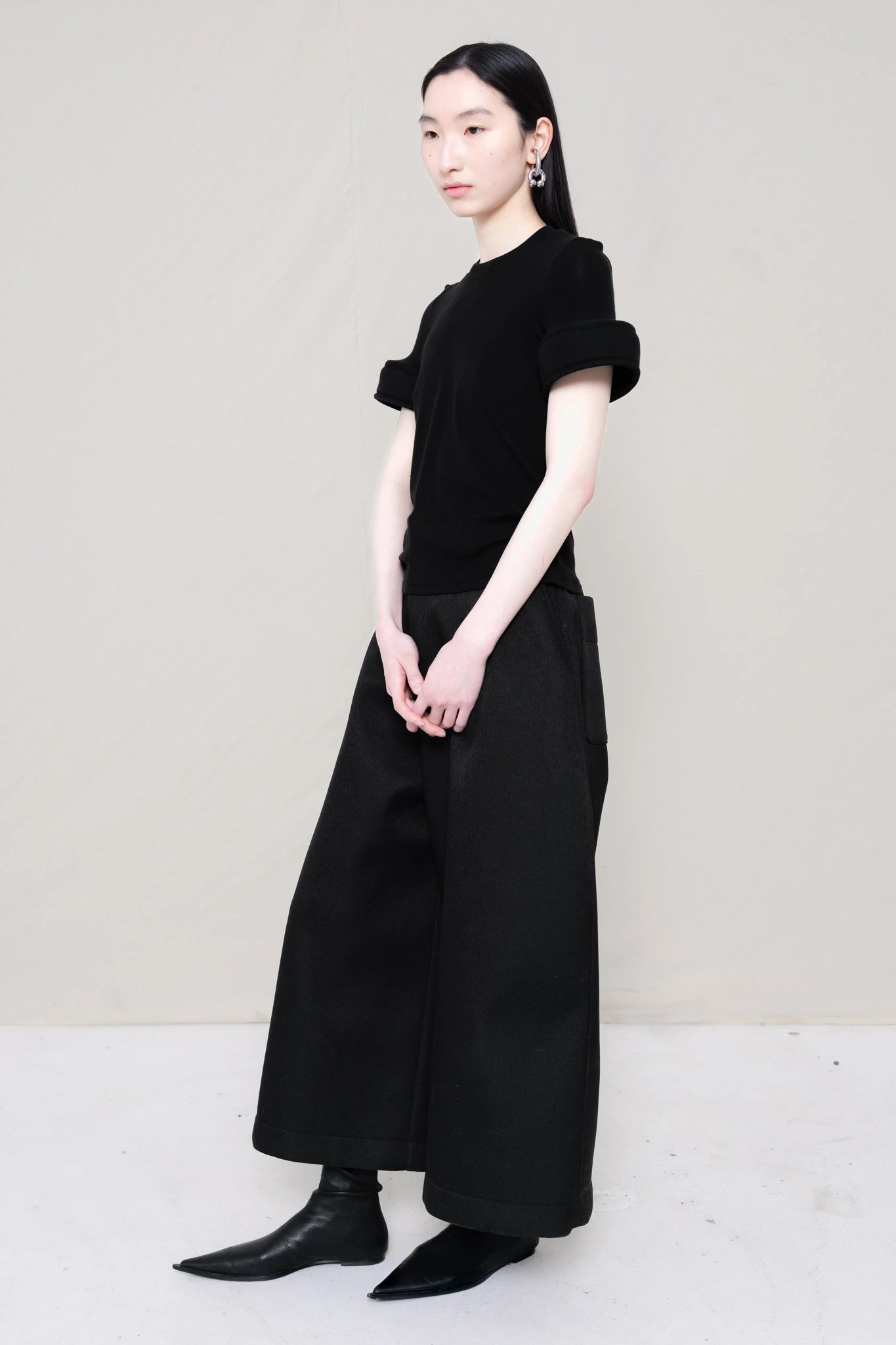 PERSON-WEARING-BLACK-TEE-WITH-FOAM-SLEEVE-CUFFS-AND-BLACK-CULOTTE-PANTS-WITH-BLACK-FLAT-POINTY-BOOTS-THREE-QUARTER-VIEW