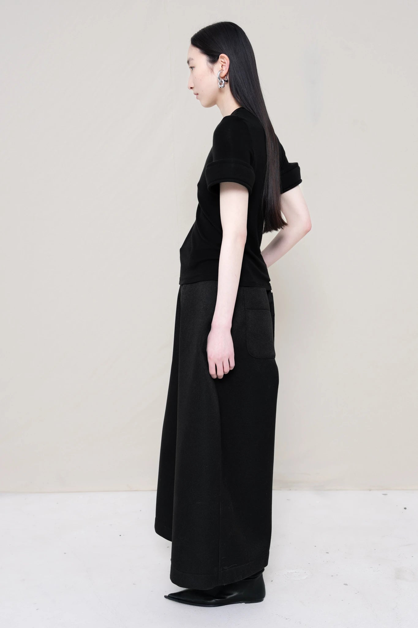 PERSON-WEARING-BLACK-TEE-WITH-FOAM-SLEEVE-CUFFS-AND-BLACK-CULOTTE-PANTS-WITH-BLACK-FLAT-POINTY-BOOTS-SIDE-VIEW
