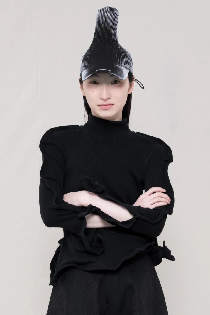 PERSON-WEARING-PAINTED-PLEAT-POINTY-CAP-WITH-BLACK-ZIG-ZAG-TOP-FEATURING-MALLEABLE-SLEEVES-PAIRED-WITH-BLACK-CULOTTE-PANTS-CLOSE-UP-FRONT-VIEW