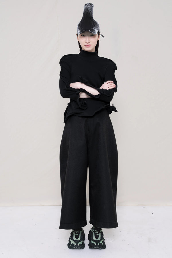 PERSON-WEARING-PAINTED-PLEAT-POINTY-CAP-WITH-BLACK-ZIG-ZAG-TOP-FEATURING-MALLEABLE-SLEEVES-PAIRED-WITH-BLACK-CULOTTE-PANTS-AND-CUSTOMIZED-SNEAKERS-FRONT-VIEW