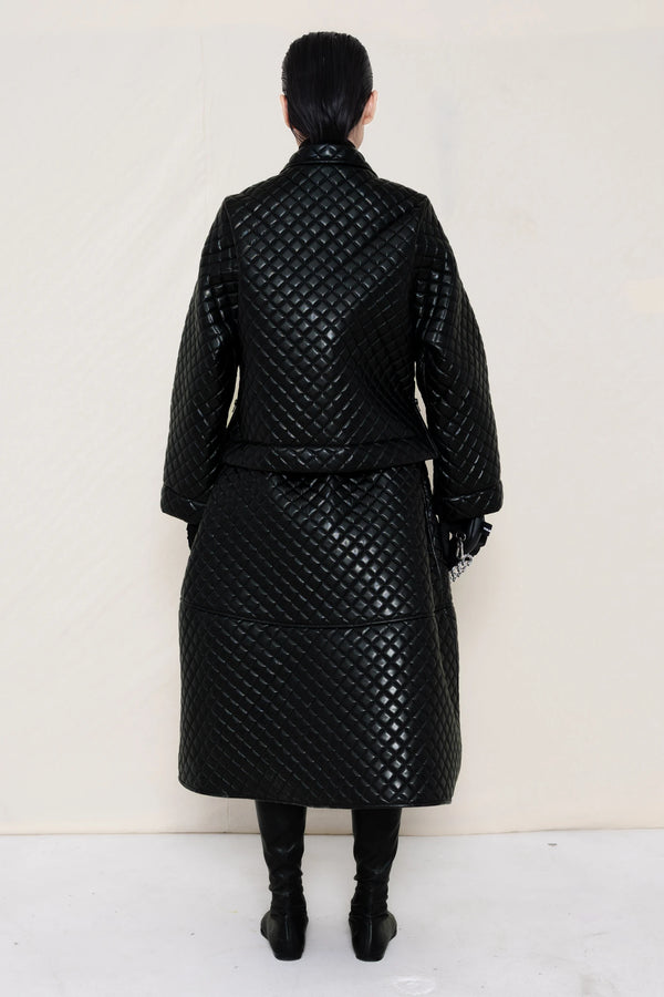 woman-wearing-a-black-quilted-jacket-over-a-black-quilted-a-line-calf-length-skirt-and-black-leather-pointed-boots-and-studded-black-leather-banana-bag-on-a-white-background-full-body-back-view