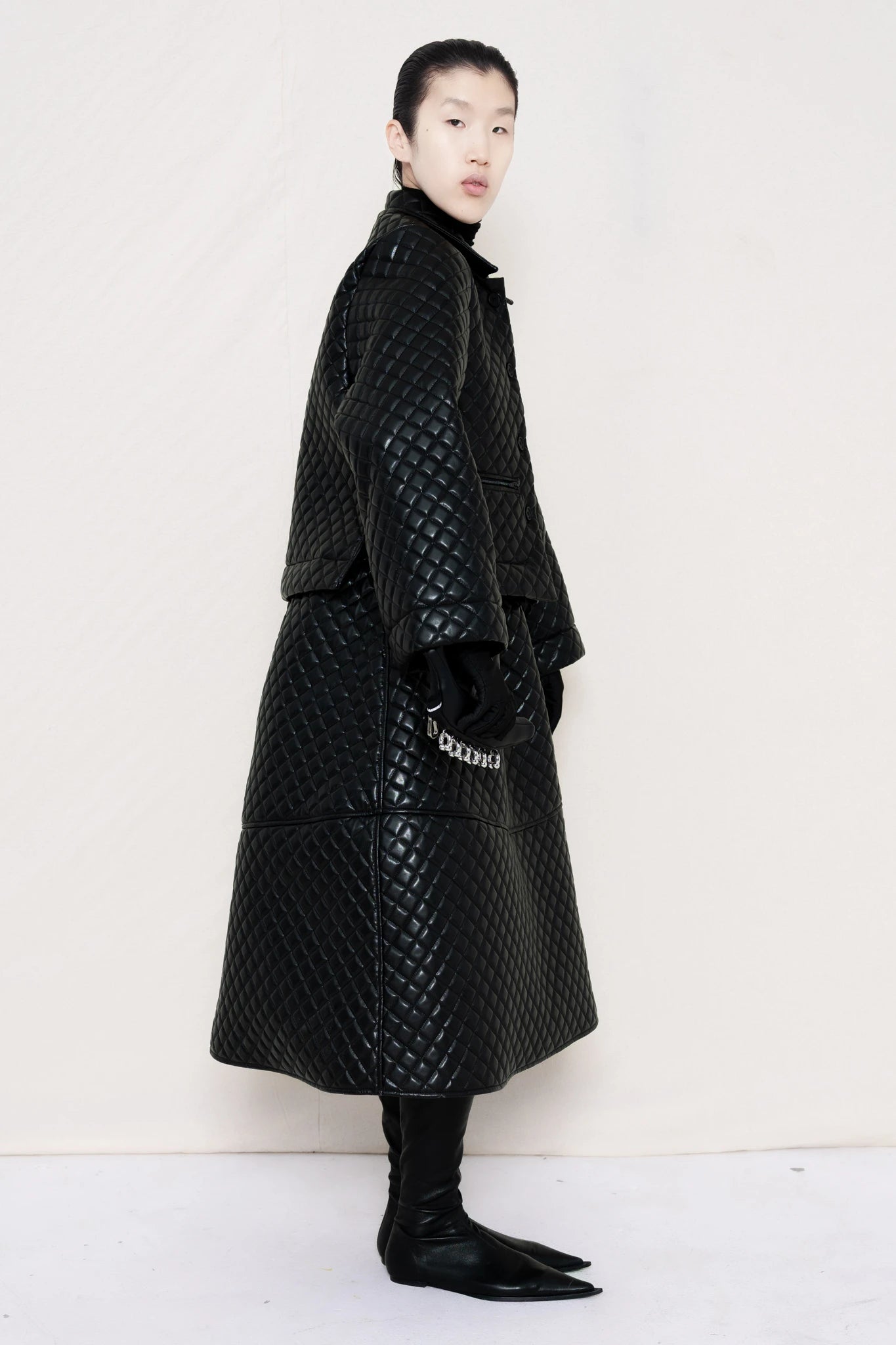 PERSON-WEARING-BLACK-QUILTED-A-LINE-SHIRT-JACKET-WITH-MATCHING-QUILTED-A-LINE-SKIRT-ACCESSORIZED-WITH-BLACK-FLAT-POINTY-BOOT-AND-PIERCED-BLACK-BANANA-TOTE-BAG-SIDE-VIEW