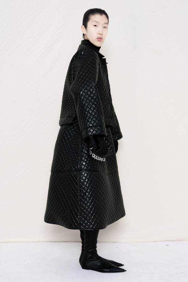 PERSON-WEARING-BLACK-QUILTED-A-LINE-SHIRT-JACKET-WITH-MATCHING-QUILTED-A-LINE-SKIRT-ACCESSORIZED-WITH-BLACK-FLAT-POINTY-BOOT-AND-PIERCED-BLACK-BANANA-TOTE-BAG-SIDE-VIEW