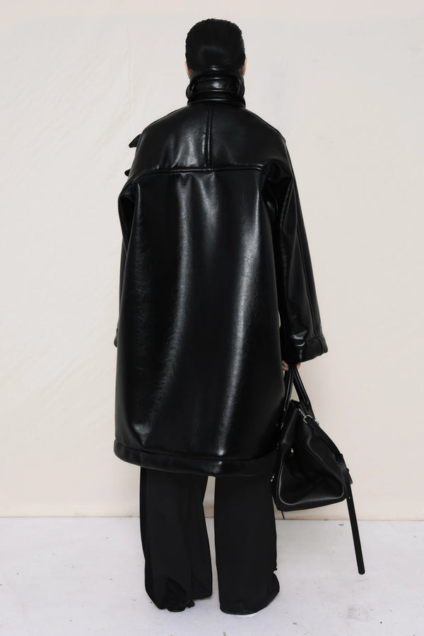 Person-wearing-a-black-shearling-oversized-coat-with- strap-and-buckle-details-worn-over-oversized-black-trousers-paired-with-a-large-black-leather-bag-and-black-pointed-leather-shoes-full-body-back-view