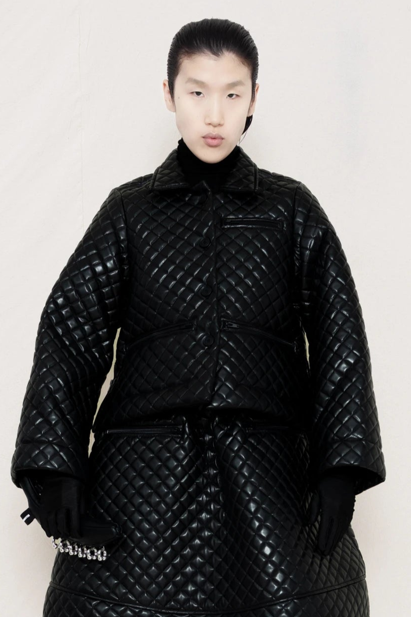 PERSON-WEARING-BLACK-QUILTED-A-LINE-SHIRT-JACKET-WITH-MATCHING-QUILTED-A-LINE-SKIRT-HOLDING-PIERCED-BLACK-BANANA-TOTE-BAG-CLOSE-UP-FRONT-VIEW