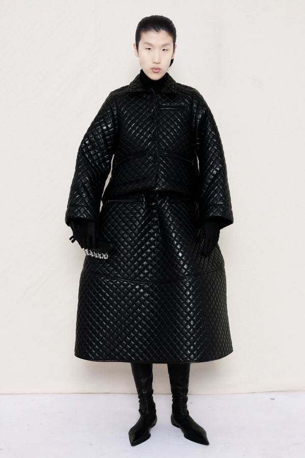 PERSON-WEARING-BLACK-QUILTED-A-LINE-SHIRT-JACKET-WITH-MATCHING-QUILTED-A-LINE-SKIRT-ACCESSORIZED-WITH-BLACK-FLAT-POINTY-BOOT-AND-PIERCED-BLACK-BANANA-TOTE-BAG-FRONT-VIEW