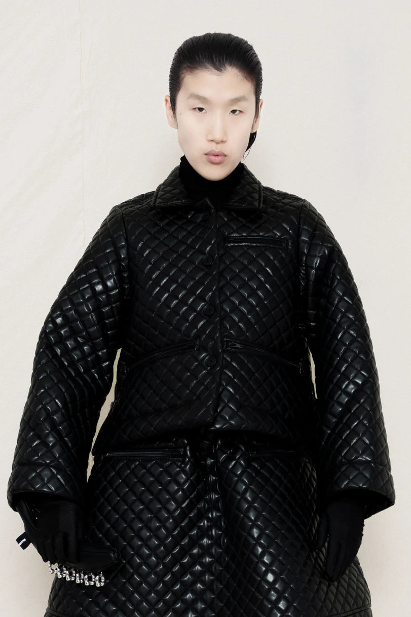 PERSON-WEARING-BLACK-QUILTED-A-LINE-SHIRT-JACKET-WITH-MATCHING-QUILTED-A-LINE-SKIRT-ACCESSORIZED-WITH-BLACK-FLAT-POINTY-BOOT-AND-PIERCED-BLACK-BANANA-TOTE-BAG-FRONT-VIEW