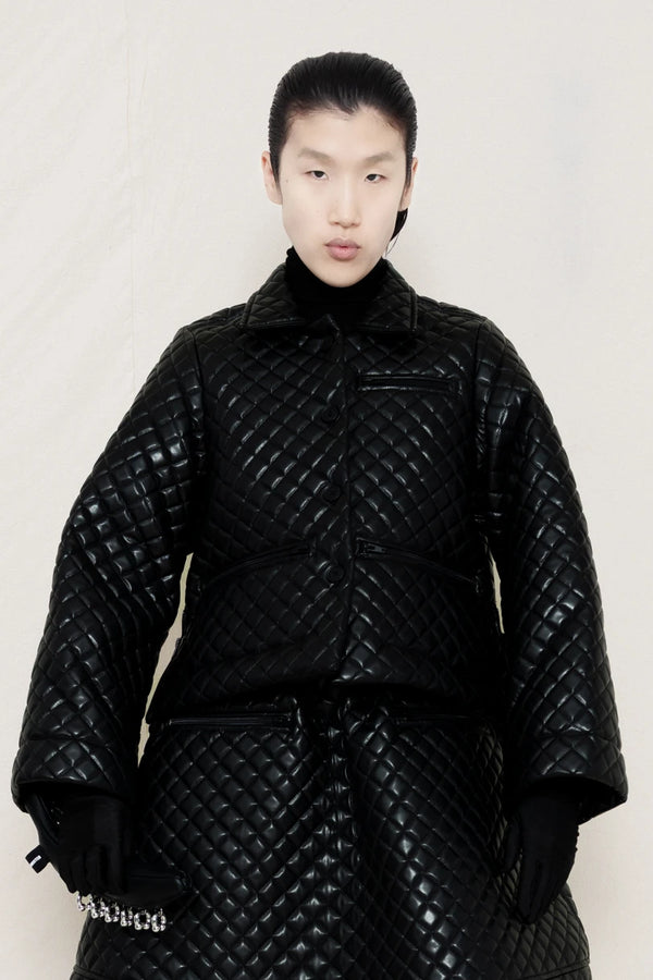 PERSON-WEARING-BLACK-QUILTED-A-LINE-SHIRT-JACKET-WITH-MATCHING-QUILTED-A-LINE-SKIRT-ACCESSORIZED-WITH-BLACK-FLAT-POINTY-BOOT-AND-PIERCED-BLACK-BANANA-TOTE-BAG-FRONT-VIEW