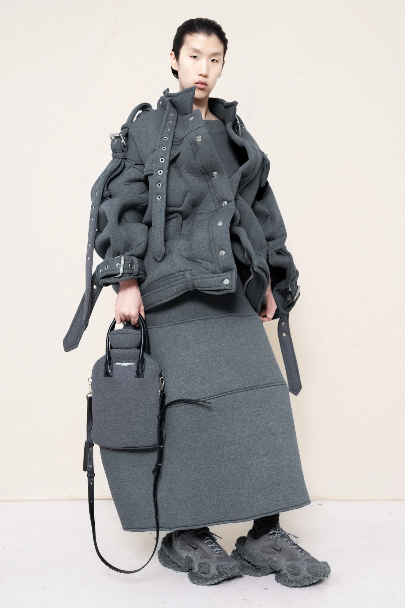 PERSON-WEARING-GREY-OVERSIZED-BELTED-JACKET-WITH-MATCHING-FOAMY-SKIRT-HOLDING-GREY-HOT-WATER-BOTTLE-BAG-AND-CUSTOMIZED-NIKE-SNEAKERS