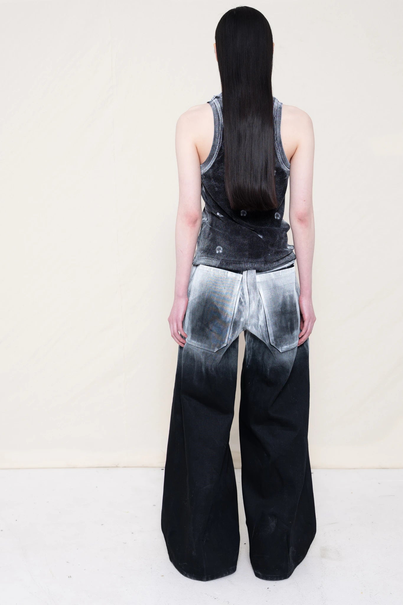 PERSON-WEARING-LONG-PAINTED-DENIM-PANTS-WITH-PAINTED-PIERCING-TANK-TOP-AND-CUSTOMIZED-SNEAKERS-BACK-VIEW