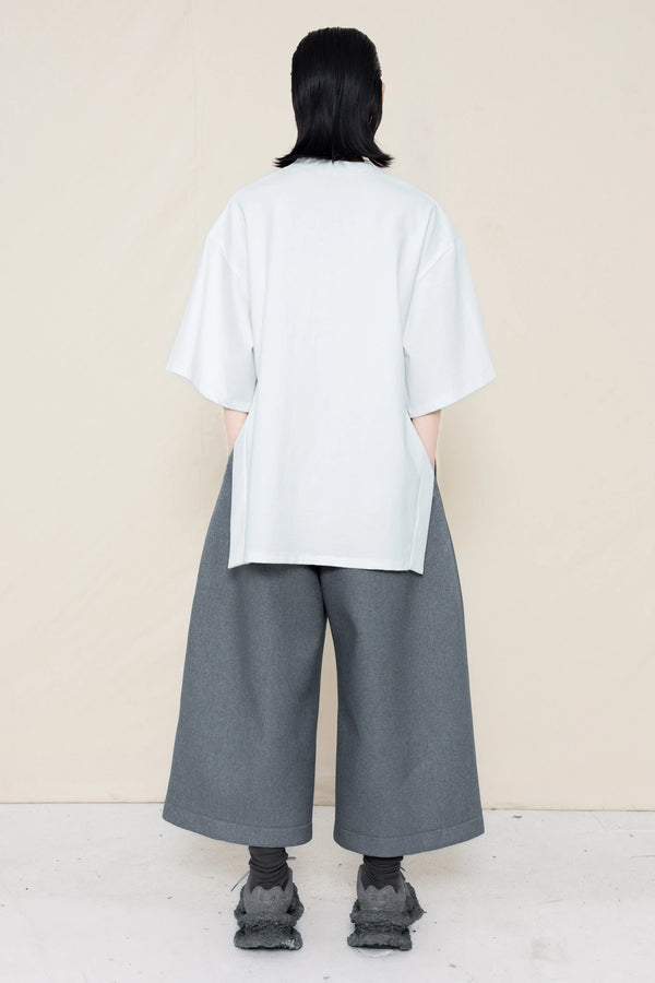 PERSON-WEARING-WHITE-TEE-WITH-SMILEY-CUT-OUT-AND-SIDE-SLIT-DETAIL-PAIRED-WITH-MELANGE-WIDE-LEG-TAILORED-WAIST-CULOTTES-AND-CUSTOMIZED-SNEAKERS-BACK-VIEW