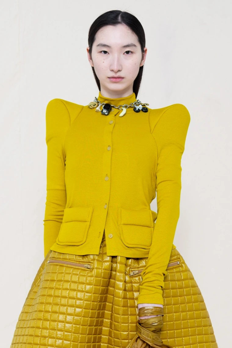 PERSON-WEARING-GOLD'ISH-FOAMY-SHOULDER-CARDIGAN-WITH-MATCHING-MOCK-NECK-SHIRT-AND-MATCHING-QUILTED-A-LINE-SKIRT-ACCESSORIZED-ON-THE-NECK-WITH-MB-CHARM-BRACELET-CLOSE-UP-FRONT-VIEW