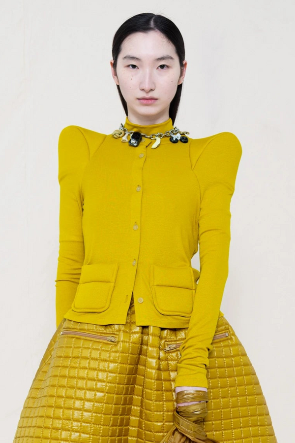 PERSON-WEARING-GOLD'ISH-FOAMY-SHOULDER-CARDIGAN-WITH-MATCHING-MOCK-NECK-SHIRT-AND-MATCHING-QUILTED-A-LINE-SKIRT-ACCESSORIZED-ON-THE-NECK-WITH-MB-CHARM-BRACELET-CLOSE-UP-FRONT-VIEW