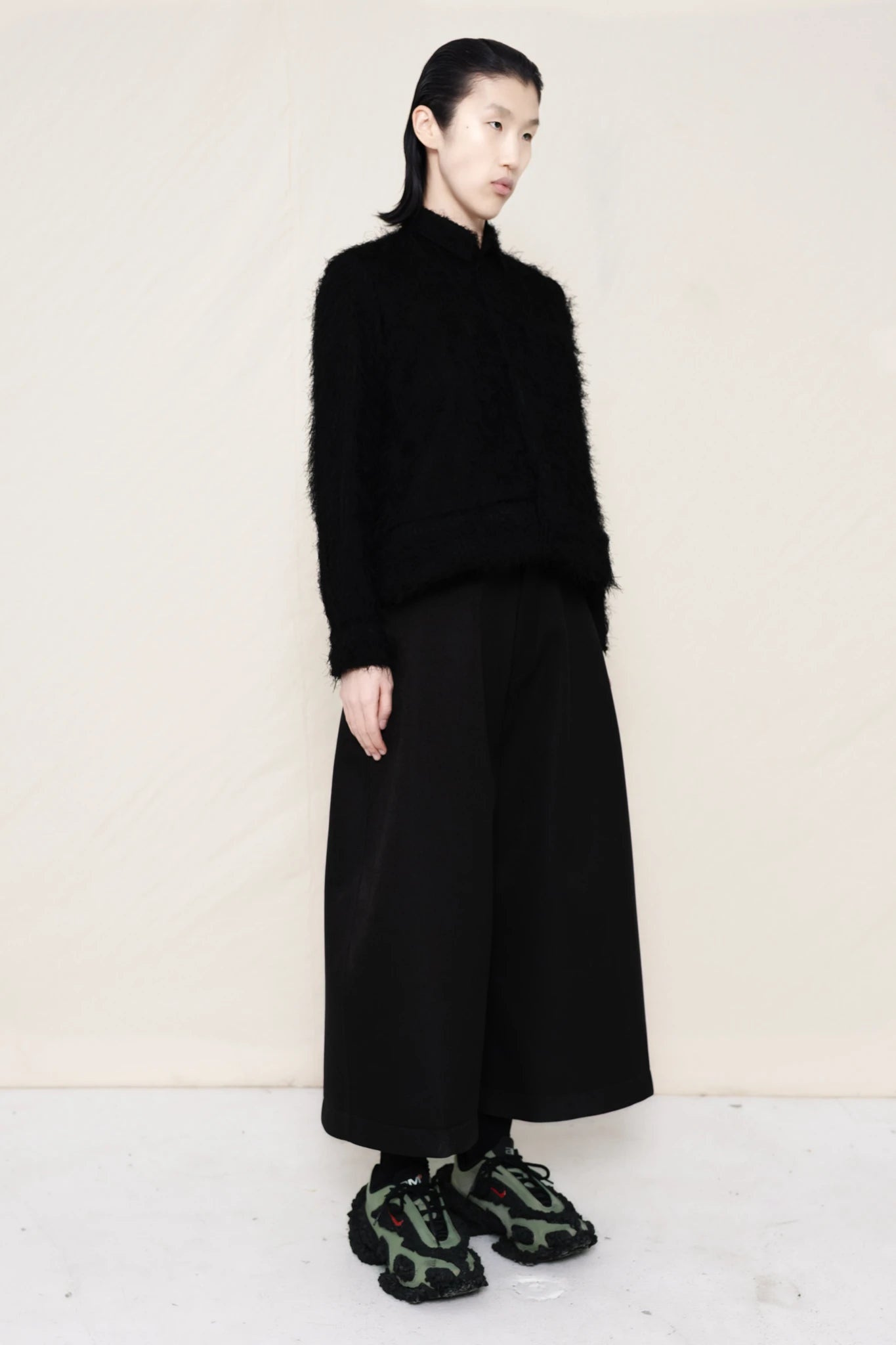 Man-wearing-A-black-COLLARED-HAIRY-JACQUARD-BUTTON-DOWN-WITH-FOAM-BOTTOM-DETAIL-over-wide-black-trousers-and-custom-shoes-against-a-plain-background-full-body-three-quarter-view