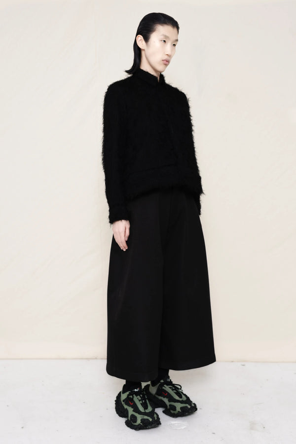 Man-wearing-A-black-COLLARED-HAIRY-JACQUARD-BUTTON-DOWN-WITH-FOAM-BOTTOM-DETAIL-over-wide-black-trousers-and-custom-shoes-against-a-plain-background-full-body-three-quarter-view