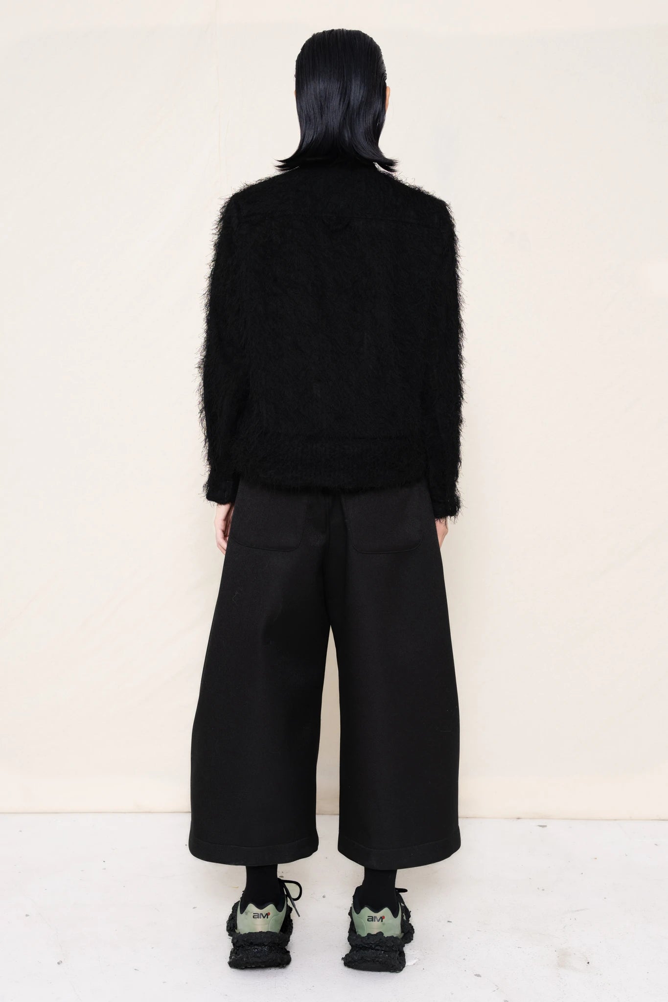 Man-wearing-A-black-COLLARED-HAIRY-JACQUARD-BUTTON-DOWN-WITH-FOAM-BOTTOM-DETAIL-over-wide-black-trousers-and-custom-shoes-against-a-plain-background-full-body-back-view