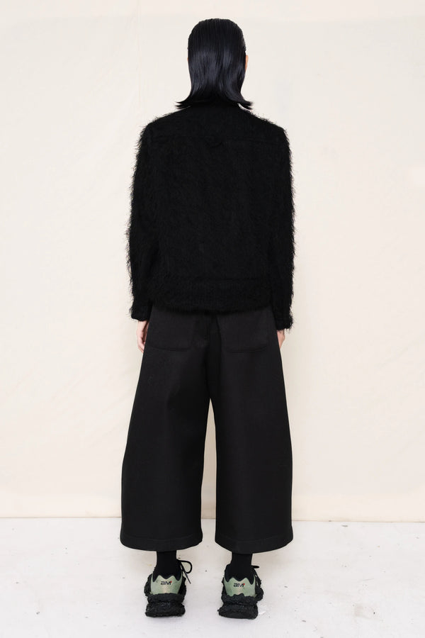 Man-wearing-A-black-COLLARED-HAIRY-JACQUARD-BUTTON-DOWN-WITH-FOAM-BOTTOM-DETAIL-over-wide-black-trousers-and-custom-shoes-against-a-plain-background-full-body-back-view