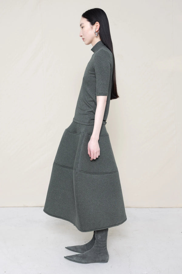 woman-wearing-A-shORT-SLEEVE-grey-BABY-MOCK-NECK-TOP-over-a-foamy-grey-dropped-waisted-o-line-skirt-with-grey-pointed-boots-against-a-plain-background-full-body-side-view