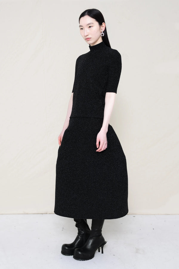 woman-wearing-a-short-sleeve-black-glitter-baby-mock-neck-top-over-a--foamy-black-glitter-dropped-waist-o-line-skirt-and-black-leather-boots-against-a-plain-background-full-body-three-quarter-view