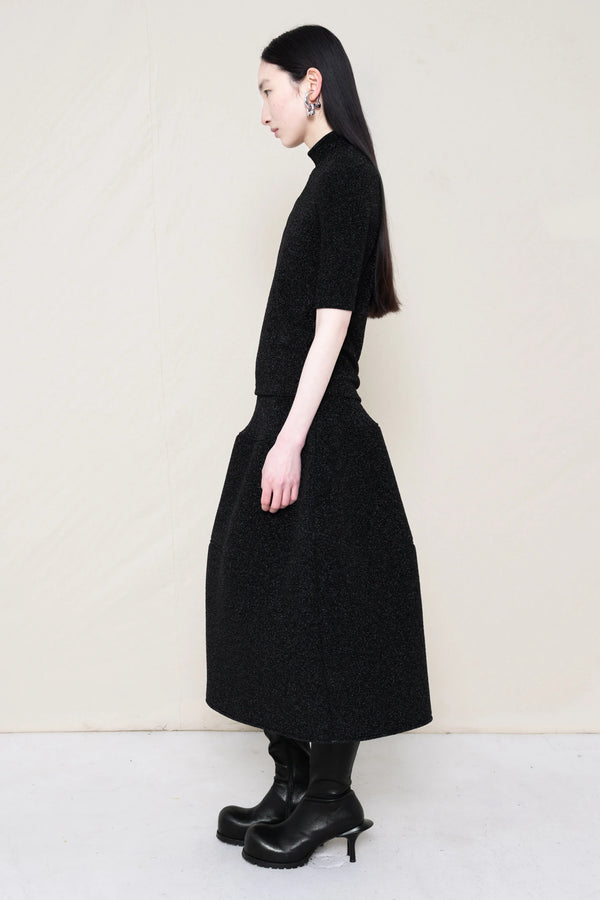 woman-wearing-a-short-sleeve-black-glitter-baby-mock-neck-top-over-a--foamy-black-glitter-dropped-waist-o-line-skirt-and-black-leather-boots-against-a-plain-background-full-body-side-view