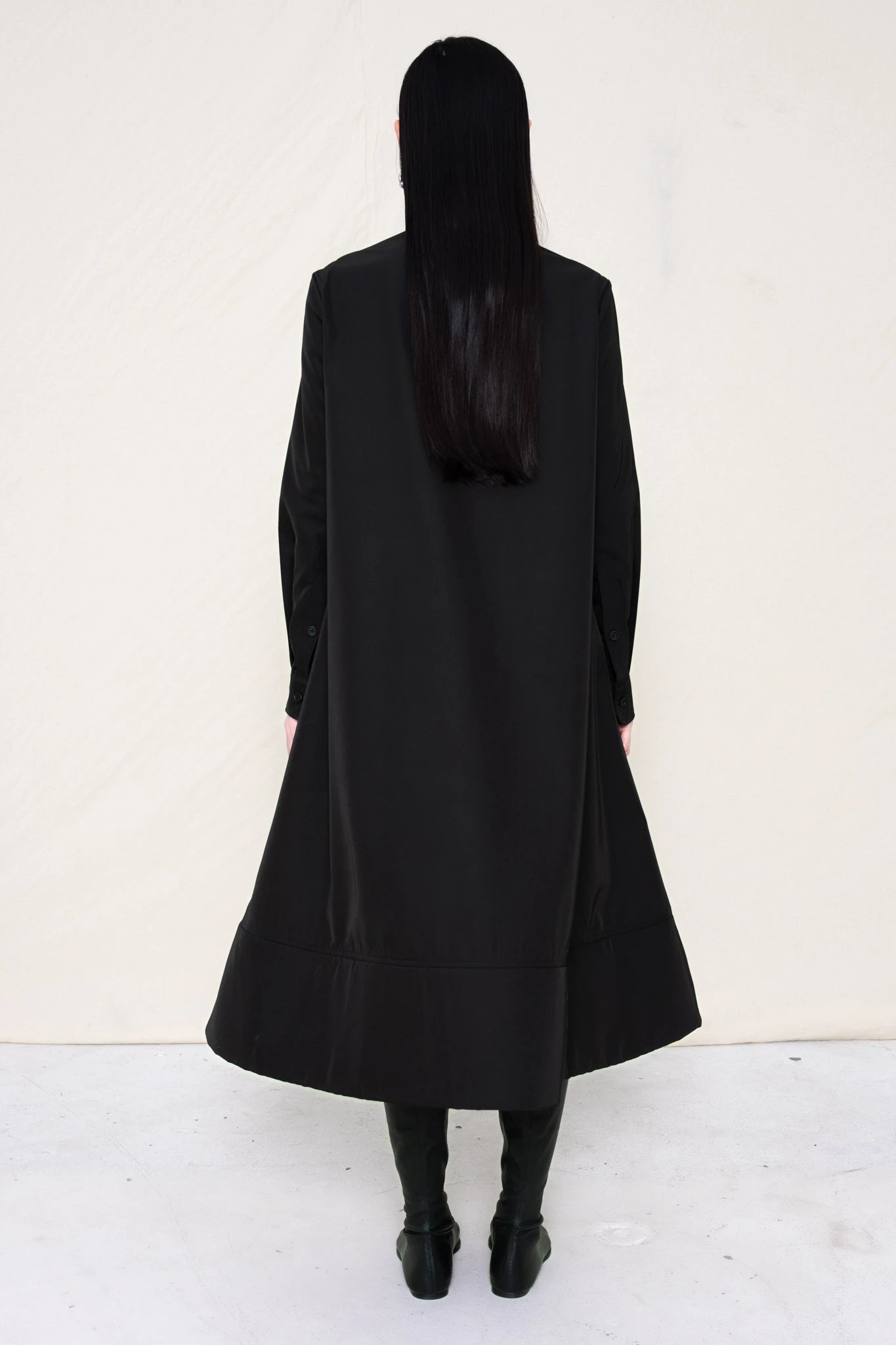 PERSON-WEARING-BLACK-COLLARED-FOAM-BOTTOM-BUTTON-DOWN-SHIRT-DRESS-WITH-BLACK-FLAT-POINTY-BOOTS-BACK-VIEW