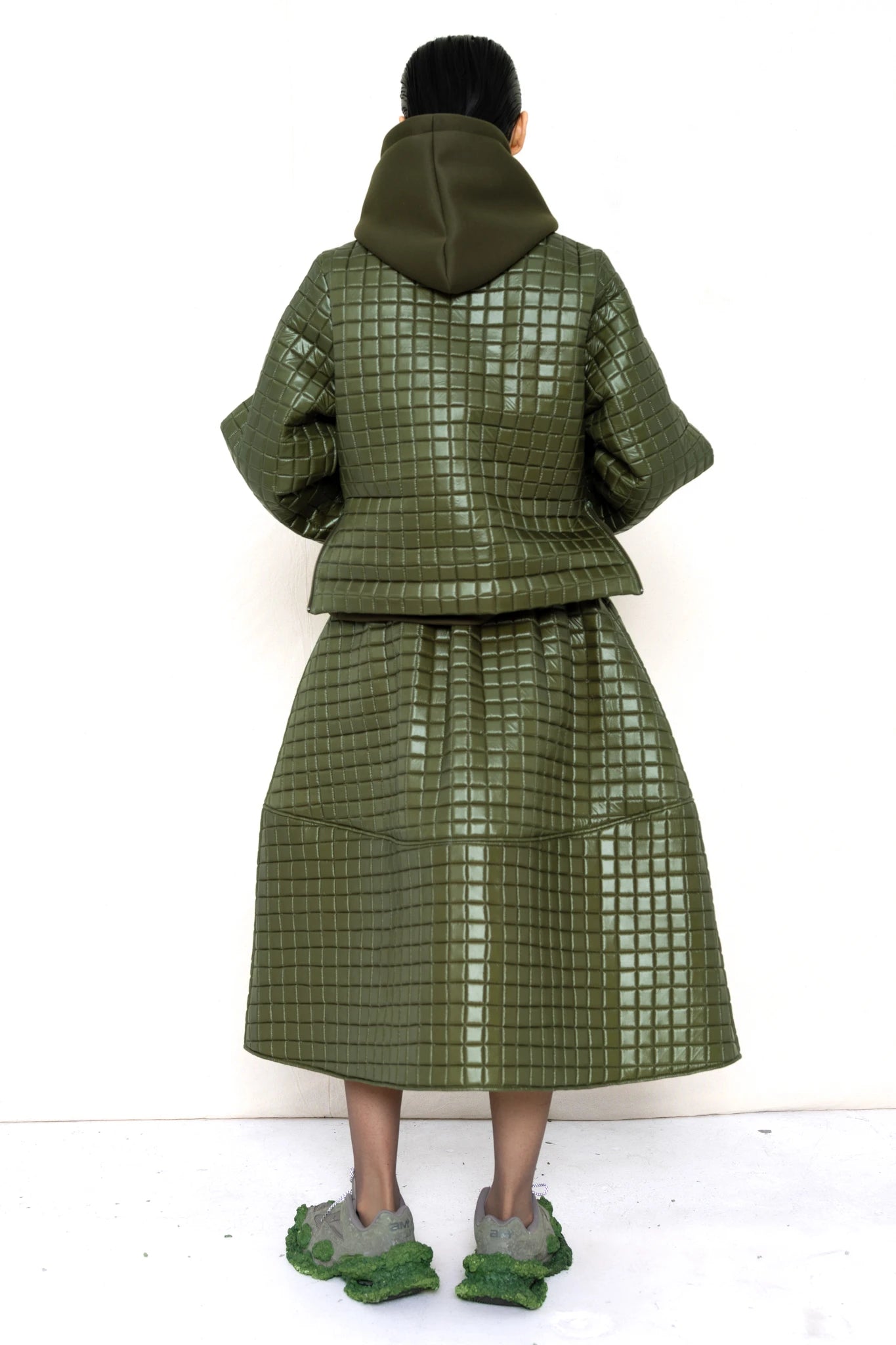 PERSON-WEARING-MOSS-GREEN-COLORED-QUILTED-JACKET-WITH-POCKETS-AND-COLLAR-OVER-MOSS-GREEN-HOODIE-WITH-MATCHING-QUILTED-A-LINE-SKIRT-AND-MUD-GREEN-COLORED-CUSTOMIZED-NIKE-SNEAKER-BACK-VIEW