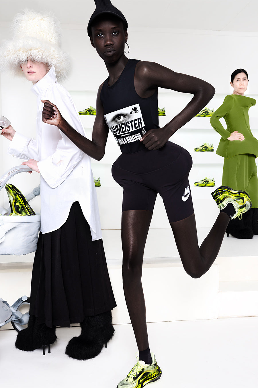Model running in front of two other models  in a white room with green shoes in shelves in the back