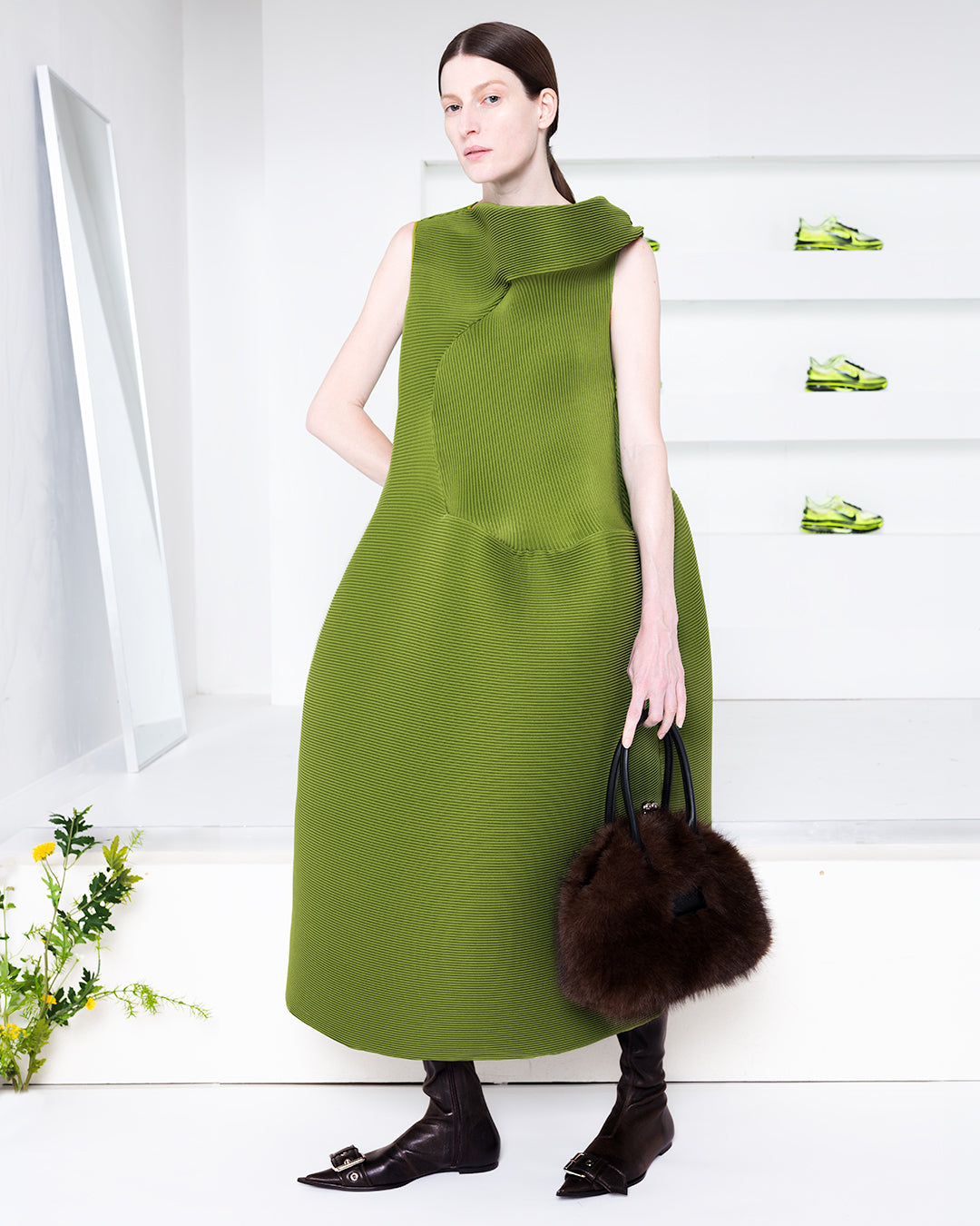 Model in a white room wearing a green dress and black boots
