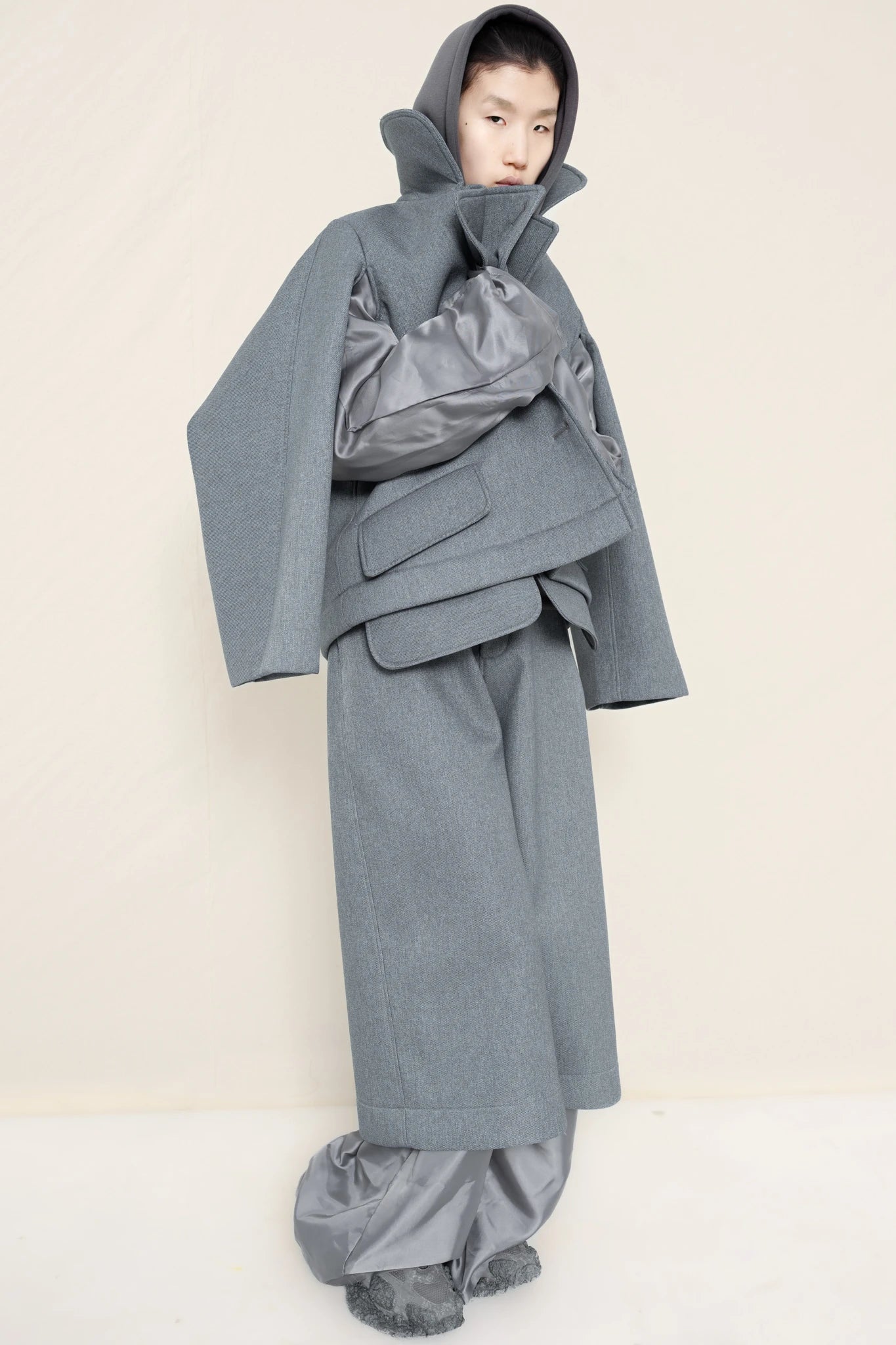 PERSON-WEARING-LAYERED-SUIT-SET-IN-MELANGE-WITH-STONE-GREY-HOODIE-UNDERNEATH-AND-CUSTOMIZED-SNEAKERS-THREE-QUARTER-VIEW