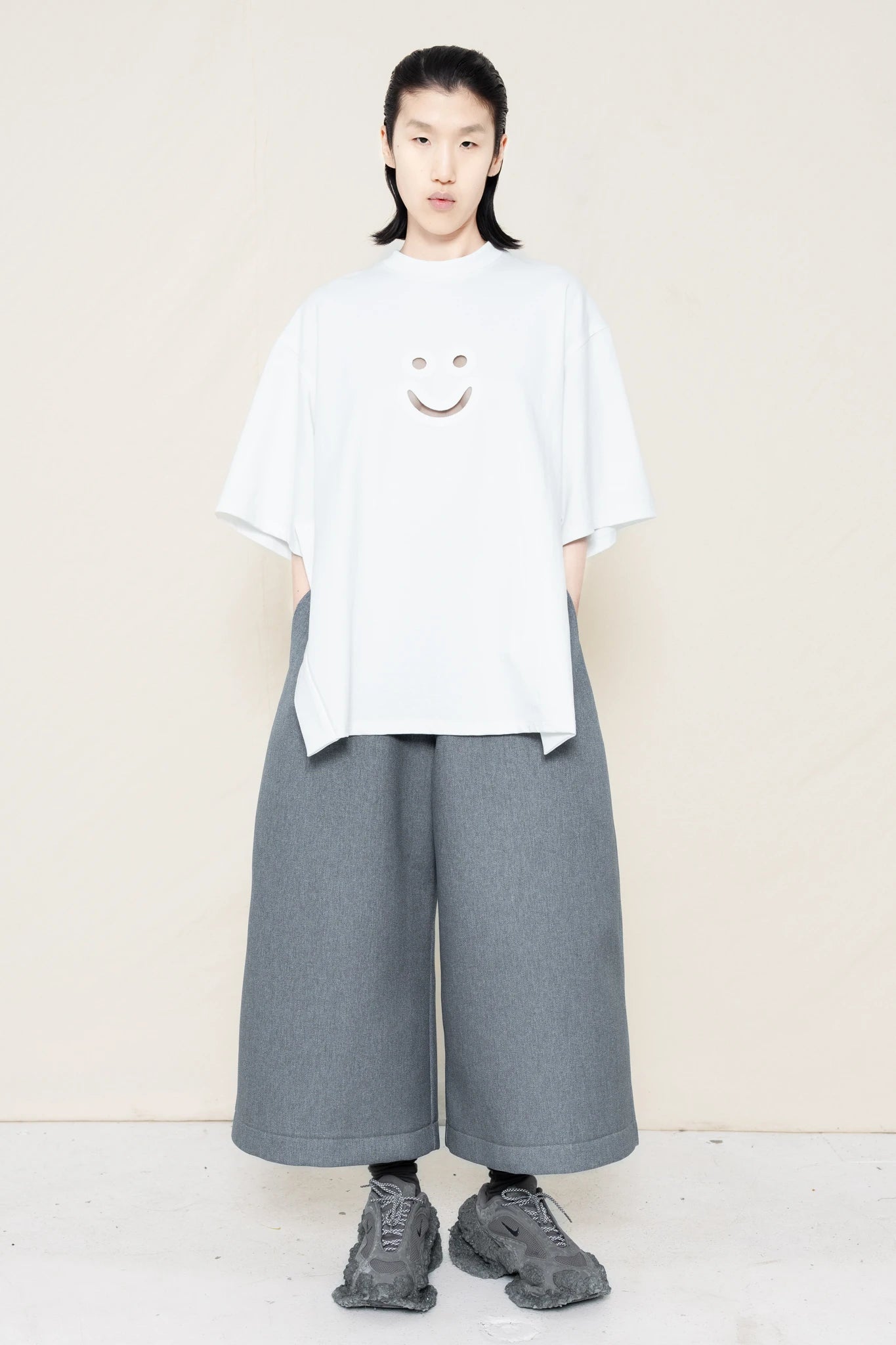 PERSON-WEARING-WHITE-TEE-WITH-SMILEY-CUT-OUT-AND-SIDE-SLIT-DETAIL-PAIRED-WITH-MELANGE-WIDE-LEG-TAILORED-WAIST-CULOTTES-AND-CUSTOMIZED-SNEAKERS-FRONT-VIEW