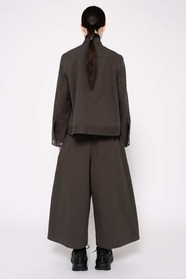 A model shown from the back wearing a dark grey cropped jacket and matching wide-leg trousers, paired with black boots, against a plain white studio background.