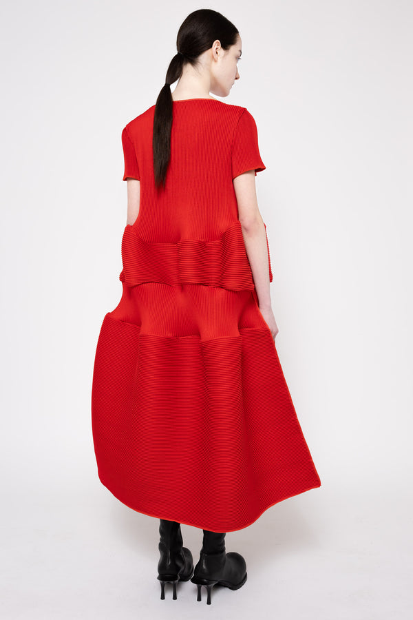 A model shown from the back wearing a bright red short-sleeved midi dress with a textured, tiered ruffled back design, paired with black high-heeled boots against a plain white studio background.