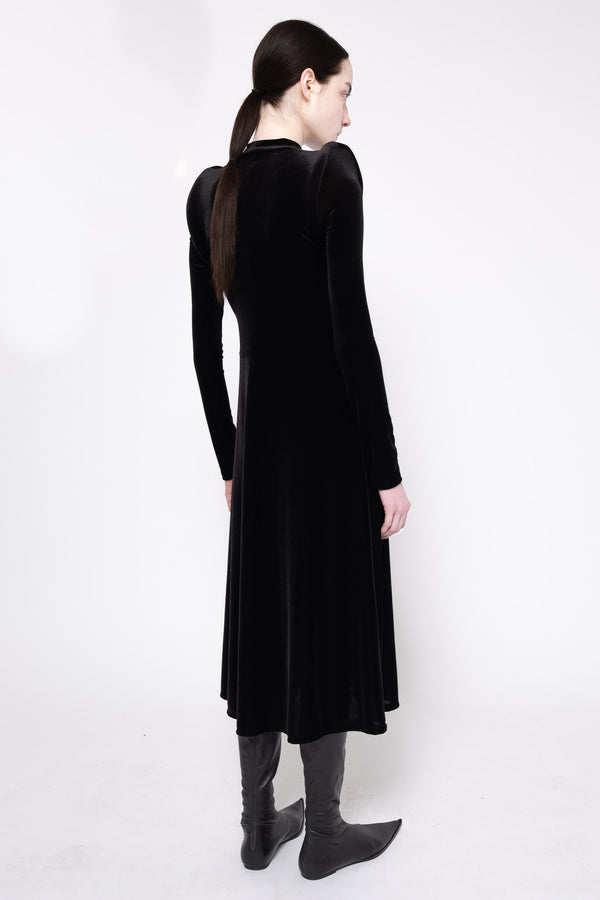 A woman wearing a long black velvet long-sleeve dress, shown from the back, paired with dark gray boots, against a plain white studio background.