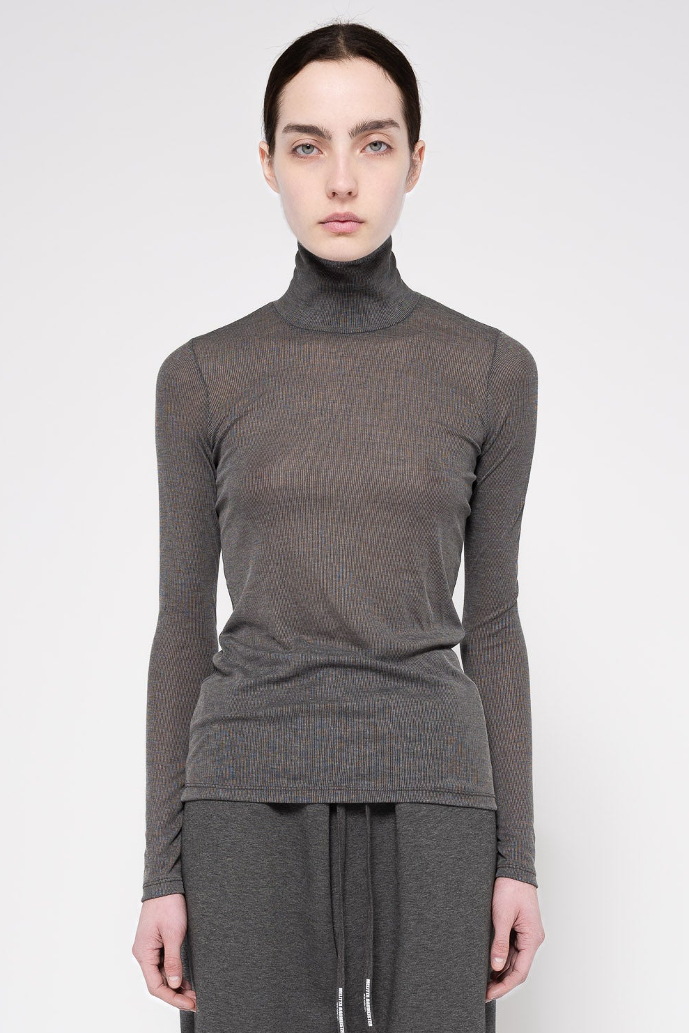 A model wearing a dark gray long-sleeve turtleneck top and matching gray drawstring pants, photographed against a light gray studio background.