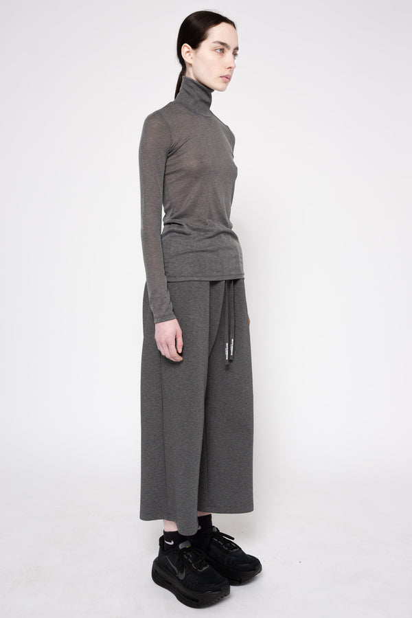 A model wearing a dark gray ribbed turtleneck sweater and matching wide-leg cropped pants with a drawstring waist, paired with black sneakers, photographed against a light gray studio background.