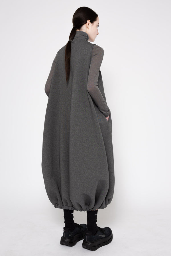A model shown from the back wearing a dark gray oversized cape-style dress with long sheer sleeves and black platform shoes, photographed against a plain white studio background.