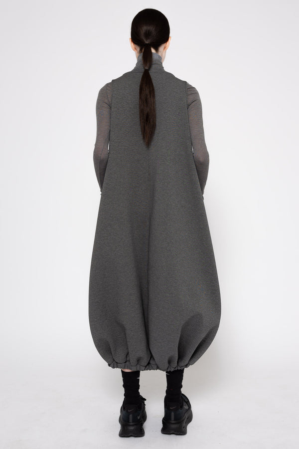 A model viewed from the back wearing a dark gray long-sleeve turtleneck dress with voluminous balloon hems and black boots, set against a plain light gray studio background.