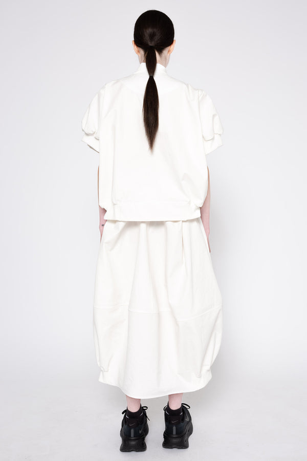 A model viewed from the back wearing a white short-sleeved top and matching wide-leg skirt, paired with black sneakers, against a plain light gray background.