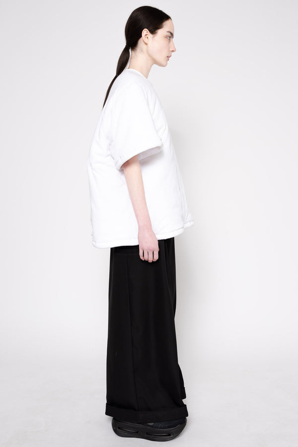 A model shown from the side profile wearing an oversized white short-sleeve t-shirt and wide-leg black trousers, standing against a plain light gray studio background.