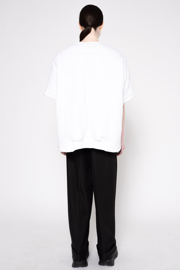 A person shown from the back wearing an oversized white short-sleeve T-shirt and loose black pants against a plain light gray studio background.