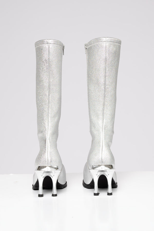 A pair of metallic silver knee-high boots with unique high heels, shown from the back on a light gray background.