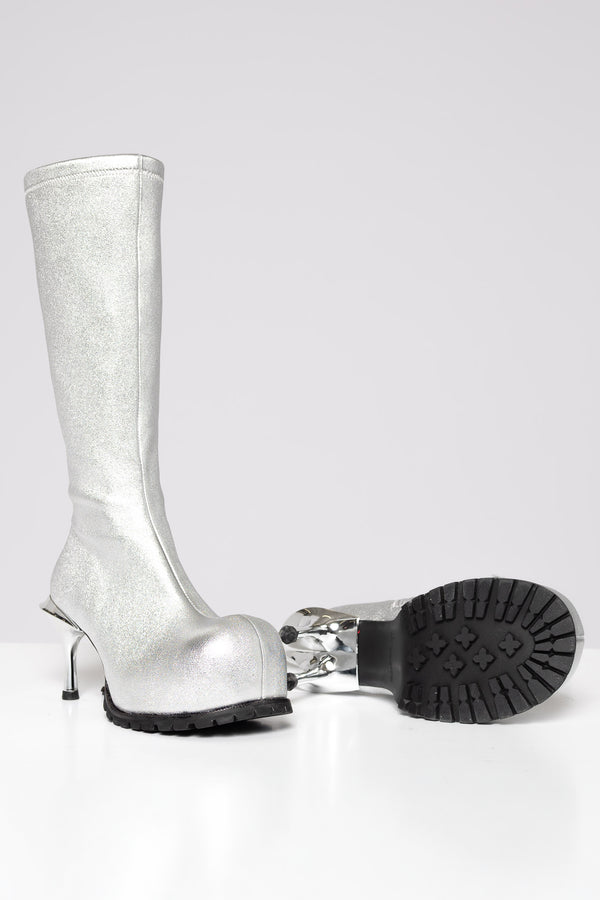 A metallic silver knee-high boot with a double high stiletto heel, shown alongside its detached black treaded sole on a light gray background.