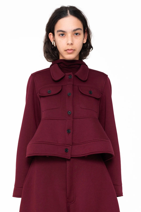 female-wearing-cropped-bordeaux-jacket-with-pockets-and-sculptural-hem-on-white-background-closeup-front
